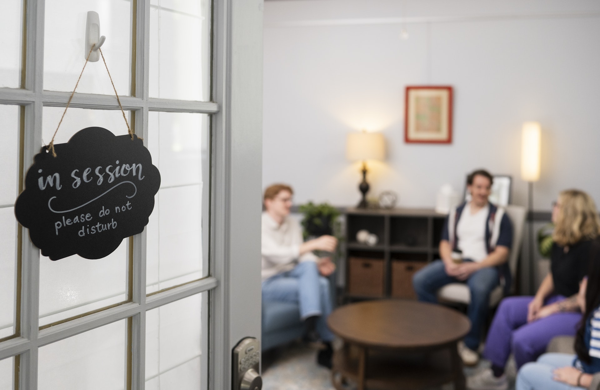 Therapy room with an “In Session – Please Do Not Disturb” sign hanging on the door, while a counseling session takes place inside. The image highlights a private, welcoming environment designed to support meaningful conversations and client confidentiality.