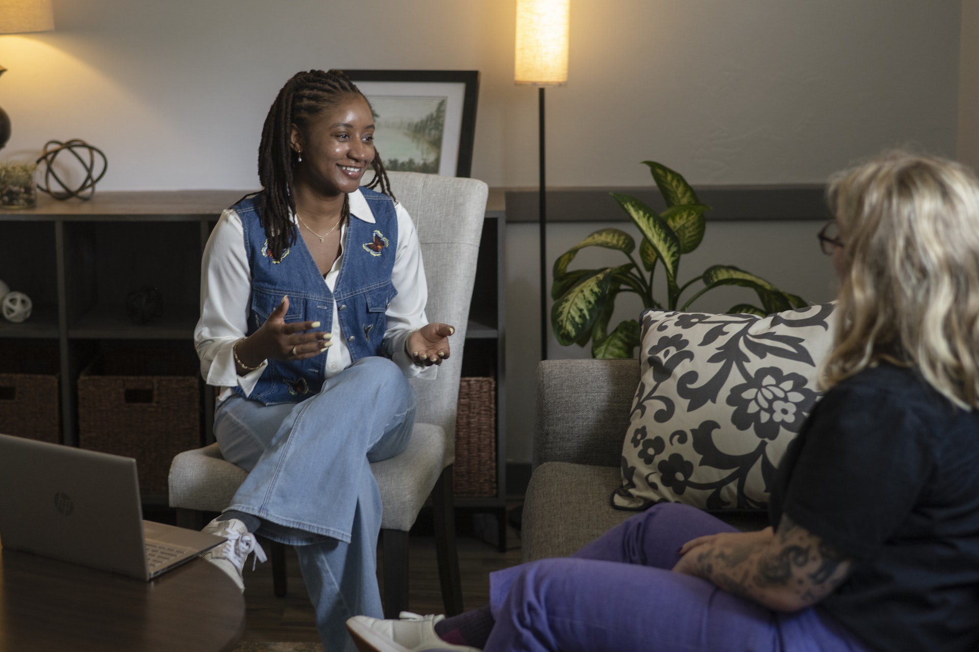 A counselor and client engage in a one-on-one conversation in a comfortable office setting, with the counselor actively listening and speaking in a supportive manner. The warm lighting, cozy furnishings, and relaxed atmosphere create a welcoming environment for guidance, connection, and personal growth.