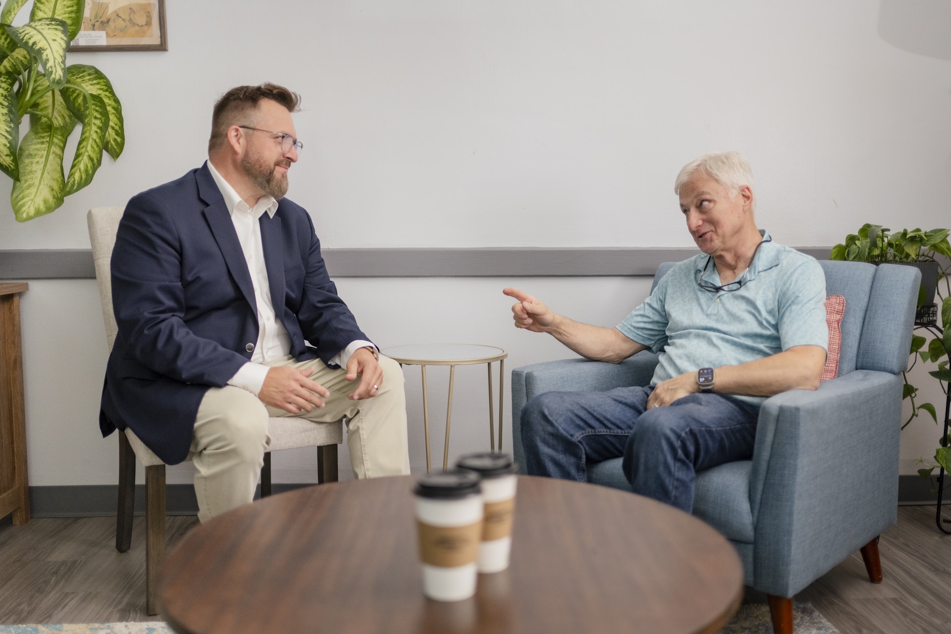 A counselor and client sit across from one another in a comfortable office, engaged in a thoughtful conversation during a counseling session. The welcoming setting, complete with cozy seating and refreshments, reflects a supportive environment focused on connection, guidance, and well-being.