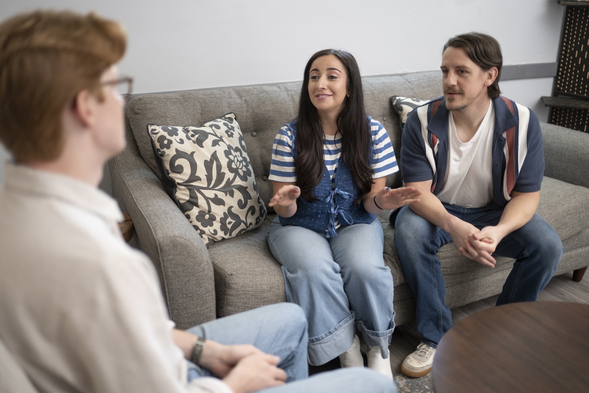 Couple participating in a counseling session, seated together on a sofa and engaged in conversation with a counselor. The welcoming setting reflects a supportive environment for relationship, marriage, or family counseling.