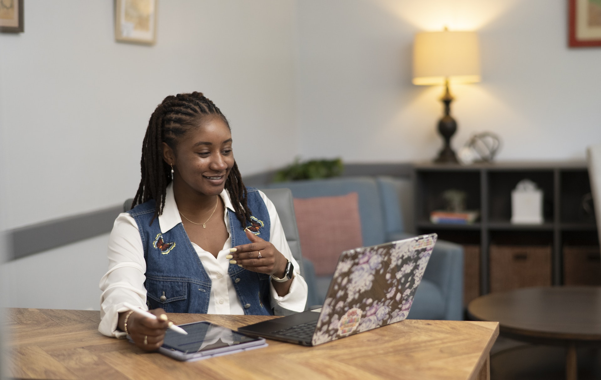 Young woman participating in a virtual counseling or coaching session, seated at a table with a laptop and tablet in a comfortable office setting. She appears engaged and attentive while speaking during an online meeting.