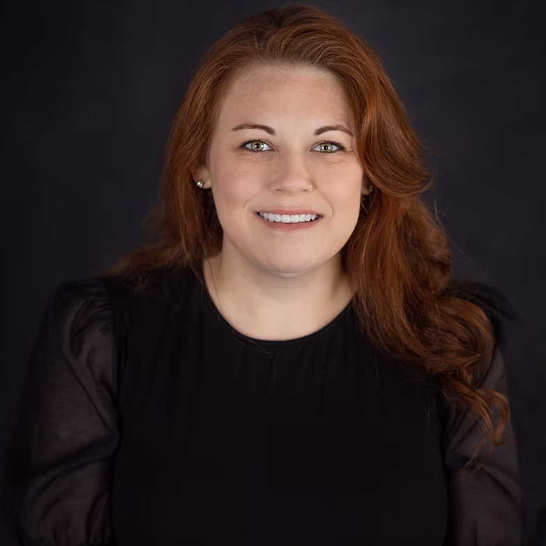 Jennifer Fleming with long red hair and a black top smiles at the camera against a dark background.